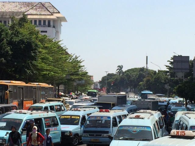 霞んだ空のジャカルタで、青い車が渋滞をなす様子の写真